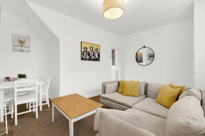 A modern living room with a sofa, a wooden table, a dining table with chairs, and wall art. - Modern 2BR House Near DLR | Isle of Dogs (London)