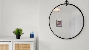 Eine weiße Wand mit einem runden Spiegel, einem Blumentopf und einem gerahmten Bild.