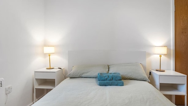 Una cama bien hecha con dos almohadas, dos mesitas de noche con lámparas y una puerta de madera.