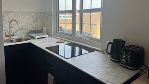 A kitchen with a sink, a stove, a toaster, and a window with a view of buildings. - Ensuite Double Room Near Clapham (London)