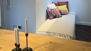 A bedroom with a bed, colorful pillows, a TV mounted on the wall, and a wooden table with candles. - Ensuite Double Room Near Clapham (London)