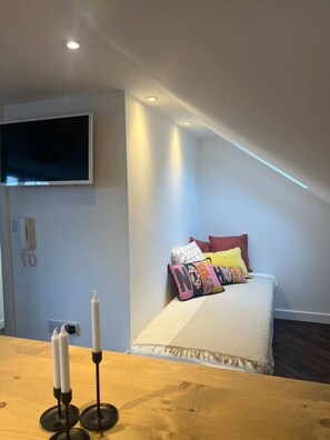 Ein Schlafzimmer mit einem Bett, bunten Kissen, einem an der Wand befestigten Fernseher und einem Holztisch mit Kerzen.