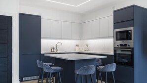 Una cocina moderna con una isla central, taburetes de bar, electrodomésticos integrados y una pared de acento oscura.
