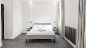 Una habitación de hotel moderna con una cama grande, mesitas de noche, un radiador y una ventana con cortinas.