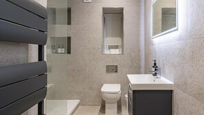 Un baño moderno con inodoro, lavamanos, espejo y zona de ducha.