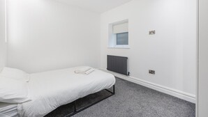 A minimalist bedroom with a single bed, a window, a radiator, and a power outlet on the wall. - Modern Brixton Flat 2 (Magherafelt)