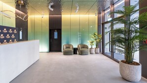 Zona de recepción con diseño moderno, que incluye un mostrador de recepción, dos espacios de descanso y una planta grande en maceta.