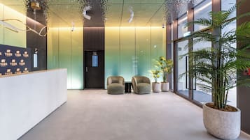 Un espace d’accueil au design moderne, comprenant un comptoir de réception, deux coins salon et une grande plante en pot.