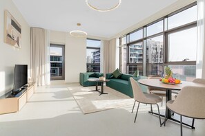 Una sala de estar moderna con un sofá, un televisor, una mesa de comedor con sillas y ventanas grandes que ofrecen vistas a la ciudad.