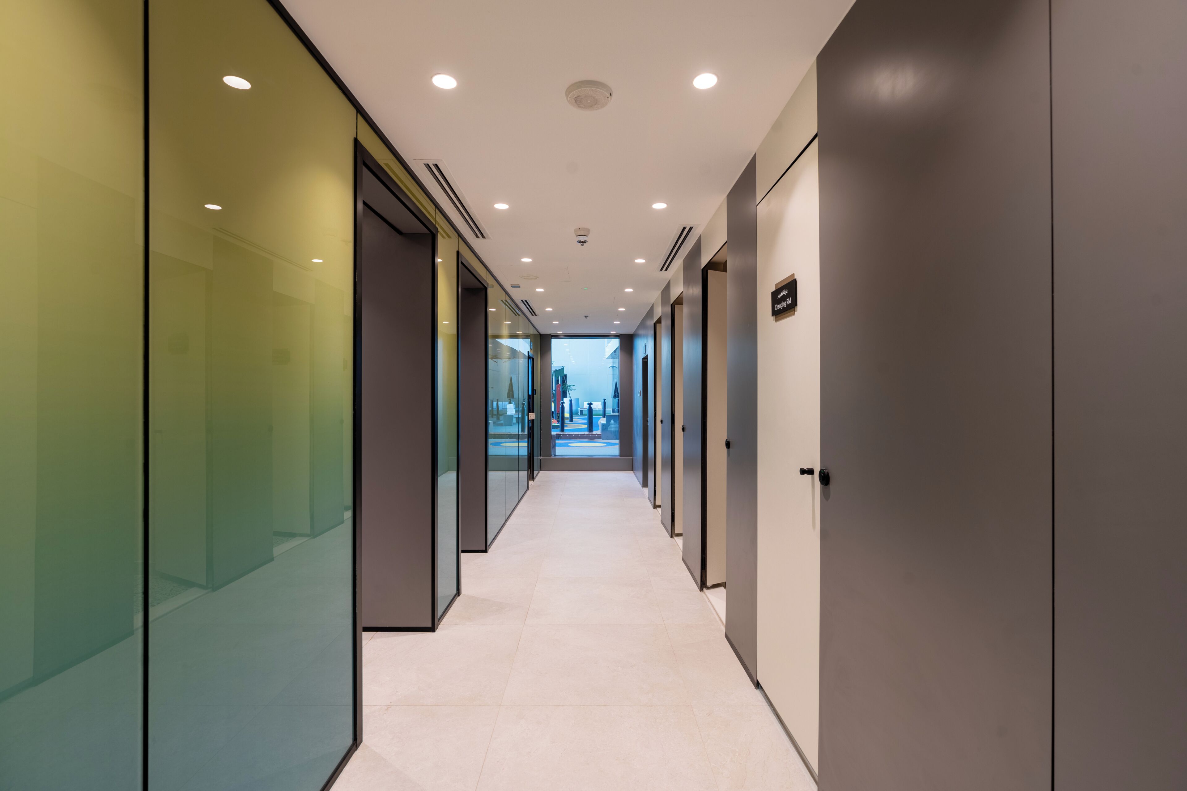 A modern hallway with glass walls, recessed lighting, and a clean, tiled floor.