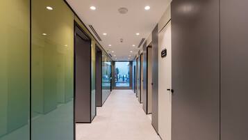 A modern hallway with glass walls, recessed lighting, and a clean, tiled floor.