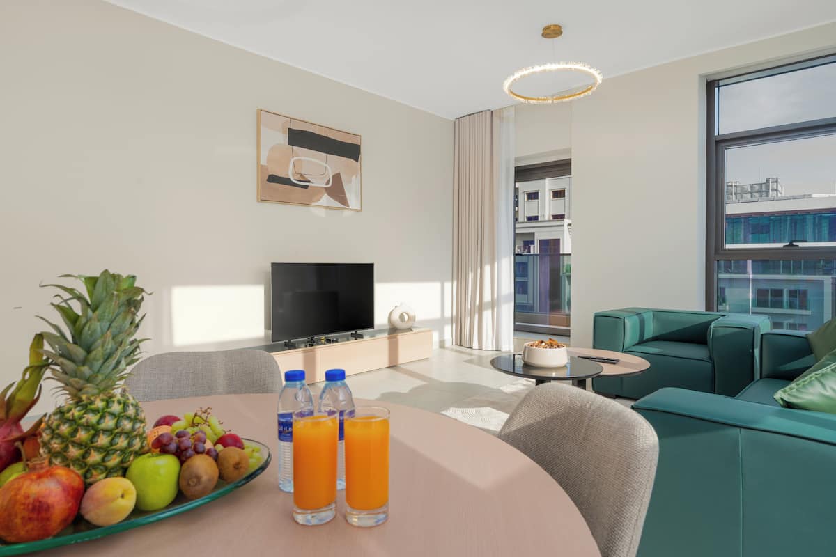 Un salon moderne avec un téléviseur à écran plat, une table à manger avec des fruits et des boissons, un canapé et une grande fenêtre.