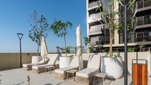 Terraza al aire libre con sillones y sombrillas, un edificio moderno con balcones y plantas en macetas.