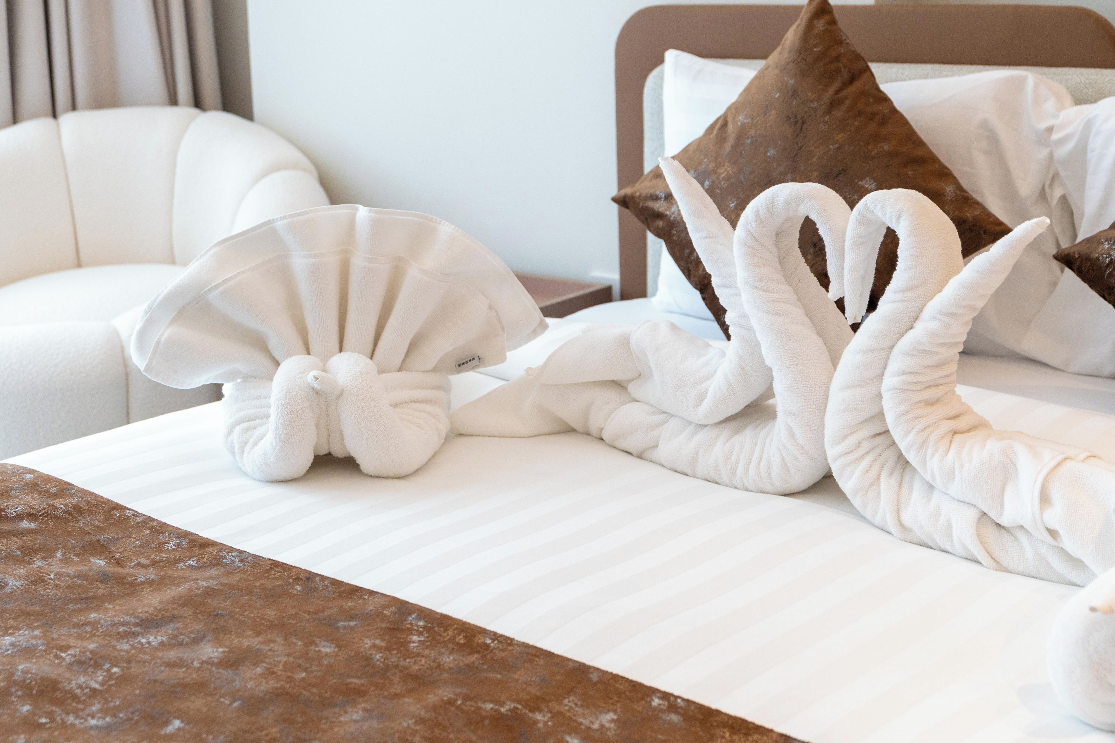 Quarto de hotel com cama bem arrumada, cabeceira marrom e cadeira branca.