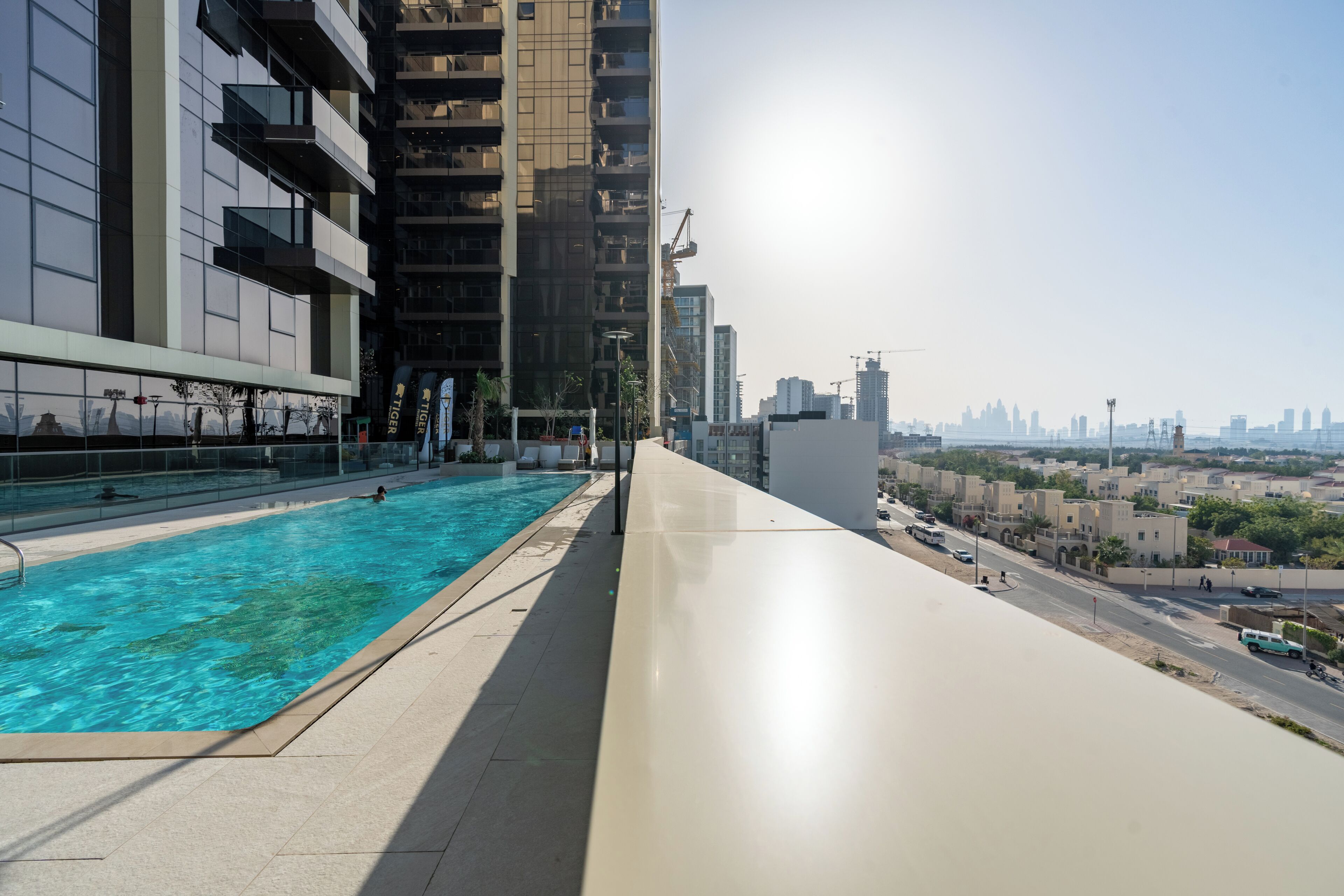 A rooftop swimming pool with a city view, modern buildings, and a clear sky.