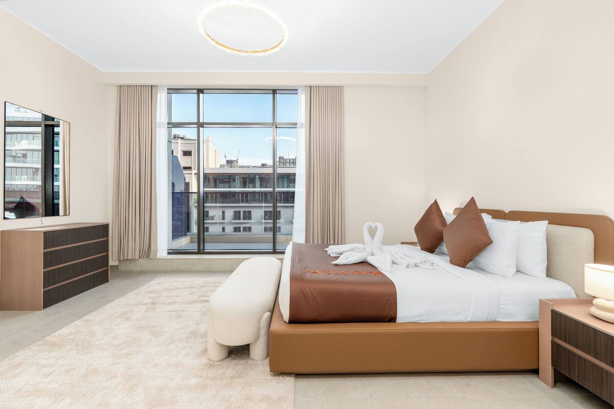 Une chambre d’hôtel moderne avec un grand lit, une table de chevet, un banc, une télévision et une vue sur la ville.