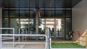 Una entrada moderna de edificio con puertas de vidrio, una escalera de metal y una barrera de cuerda roja.