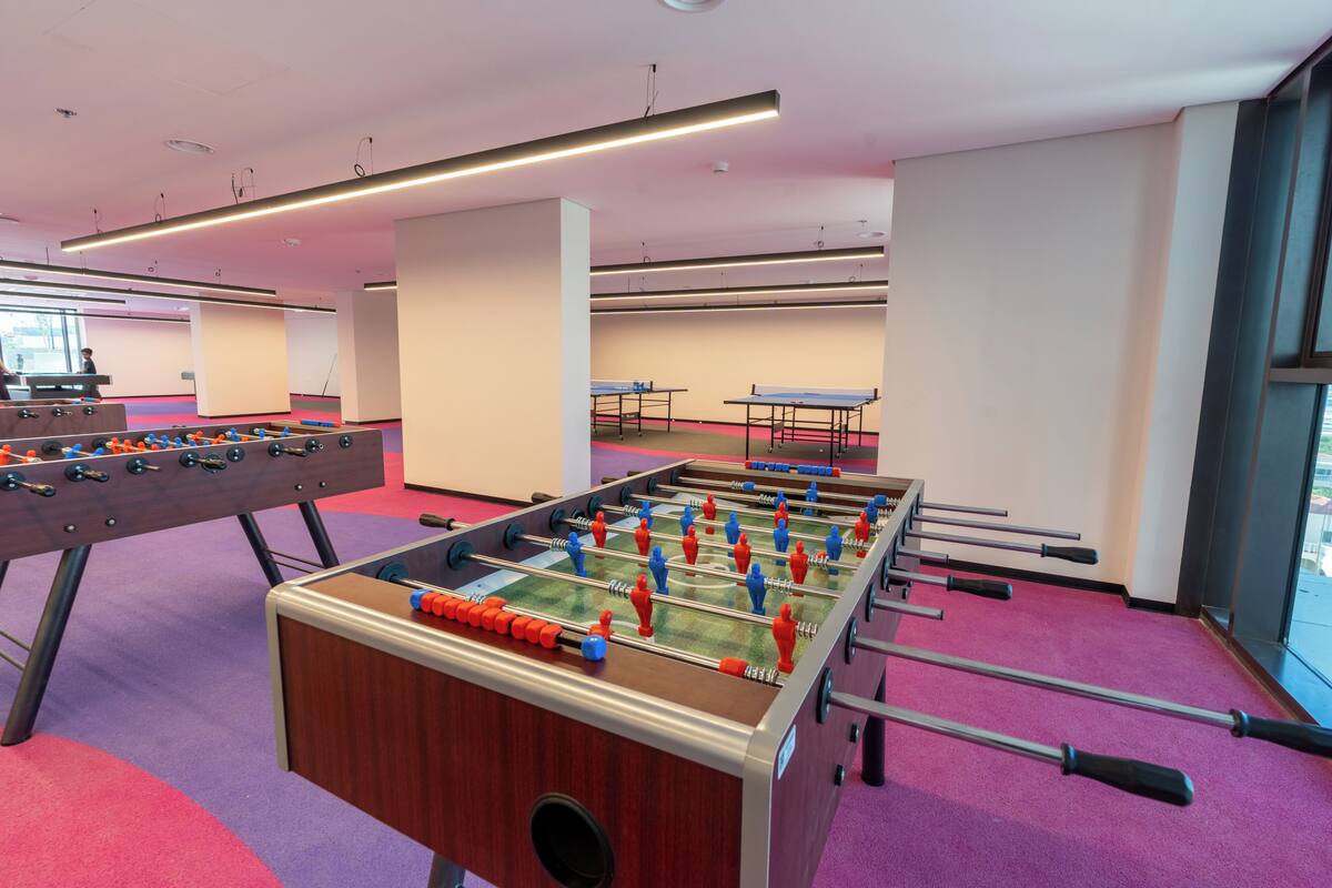 Une pièce comprenant plusieurs tables de baby-foot, une table de ping-pong et un baby-foot dont les billes sont disposées en alternance de couleurs rouge et bleue.