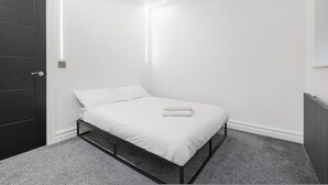 Ein schlicht eingerichtetes Schlafzimmer mit Bett, einer dunklen Tür und einer Heizung.