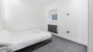 Ein schlicht eingerichtetes Schlafzimmer mit einem Bett, einem Fenster, einer Heizung und einer Steckdose.