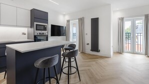 A modern kitchen with a central island, bar stools, a flat-screen TV, and a sliding glass door leading to a balcony. - Modern Brixton Flat 8 (Magherafelt)