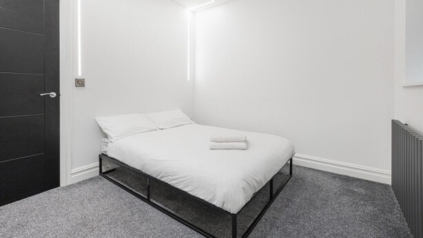 A minimalist bedroom with a bed, a door, and a radiator. - Modern Brixton Flat 8 (Magherafelt)