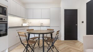 A modern kitchen with white cabinets, a round dining table, and foldable chairs. - Modern Brixton Flat 3 (Magherafelt)