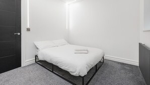 A minimalist bedroom with a bed, a dark door, and a radiator. - Modern Brixton Flat 3 (Magherafelt)
