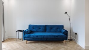 A room with a blue sofa, a small side table, a floor lamp, and a light-colored wooden floor. - Modern Brixton Flat 4 (Magherafelt)