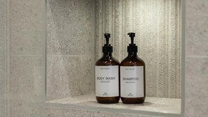 A bathroom with a built-in shelf containing two bottles of body wash and shampoo. - Modern Brixton Flat 4 (Magherafelt)