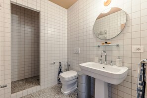 Ein Badezimmer mit weißen Fliesen, einem weißen Waschbecken und einem Spiegel darüber sowie einer Toilette.