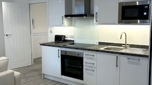 A modern kitchen with white cabinetry, a built-in oven, a microwave, and a stainless steel sink. - Charming Flat on High Street Ken (London)