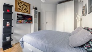 Un dormitorio con cama, armario blanco, estantería negra y un póster enmarcado en la pared.