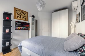 Ein Schlafzimmer mit einem Bett, einem weißen Kleiderschrank, einem schwarzen Regalsystem und einem gerahmten Poster an der Wand.