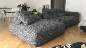 Una sala moderna con un sofá gris, una mesa de comedor con sillas y una puerta gris.