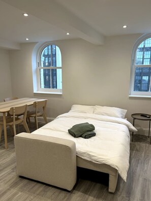 Ein Schlafzimmer mit einem Bett, einem Schreibtisch und zwei Fenstern.