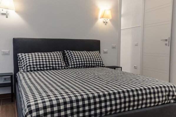 Ein Bett mit kariertem Überwurf, zwei Nachttischlampen, ein Nachttisch und eine weiße Tür.