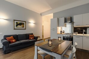 Eine moderne Küche mit weißen Schränken, einem Esstisch mit Stühlen und einem Sofa mit Kissen.