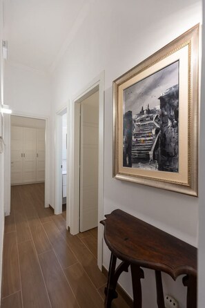 Ein Flur mit einem in Schwarzweiß gerahmten Foto an der Wand, einer hölzernen Bank und einer weißen Tür, die zu einem Raum führt.