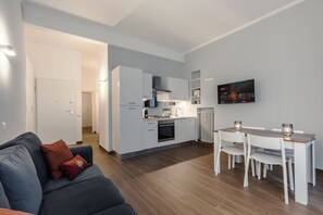 Eine moderne Küche mit weißen Schränken, ein Essbereich mit Tisch und Stühlen sowie ein Wohnzimmer mit einer Couch.