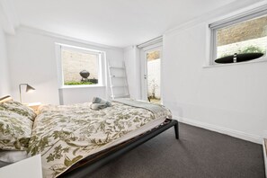 Ein Schlafzimmer mit Bett, Fenster mit Blick auf eine Ziegelwand, einer Leiter und einem Regal mit einer Pflanze.