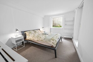 A bedroom with a bed, bedside tables, a window with a view, and built-in shelving. - Chelsea 1-bed Flat With Patio (London)