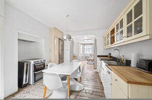A modern kitchen with white cabinetry, a wooden countertop, and a dining area with a white table and chairs. - Chelsea 1-bed Flat With Patio (London)