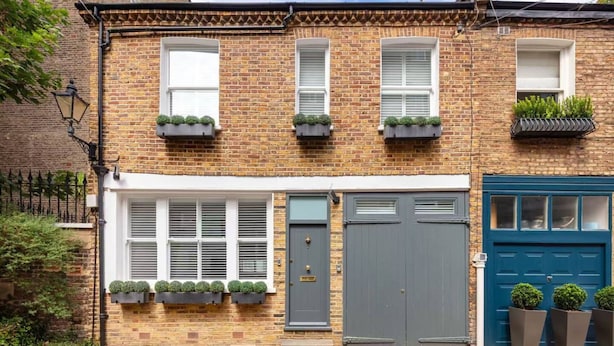 A two-story brick townhouse with a grey front door, white-framed windows, and a blue garage door. - Charming Mews House in Kensington (London)