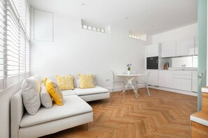 A modern apartment with a white sofa, a dining table, and a kitchen area. - Charming Mews House in Kensington (London)