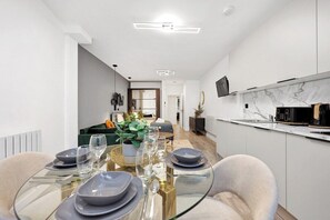 A modern kitchen with a marble countertop, a dining area with a glass table, and a living space with a sofa and plants. - Studio Flat in Central Islington | Own Patio (London)