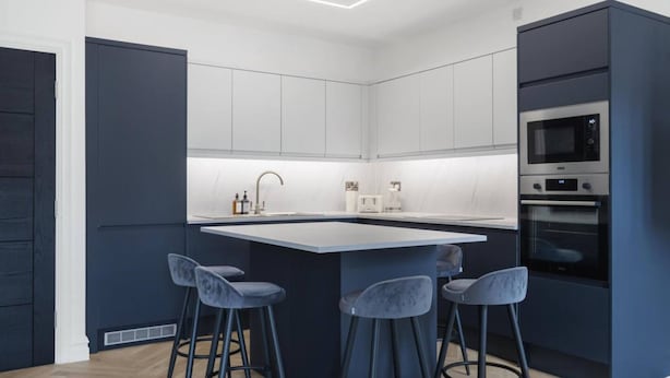 A modern kitchen with a central island, bar stools, built-in appliances, and a sleek design. - Spacious Flat in Trendy Brixton (London)