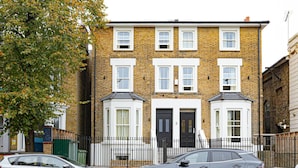 A two-story brick house with a black door, white-framed windows, and a small bay window on the second floor. - Spacious Flat in Trendy Brixton (London)