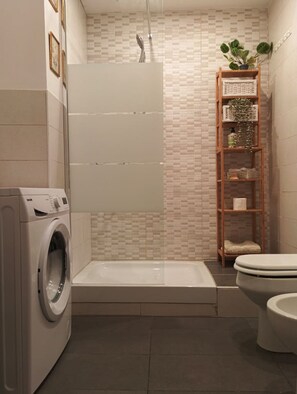 Ein modernes Badezimmer mit Waschmaschine, Duschkabine, Toilette und einer Holzablage mit Pflanzen.