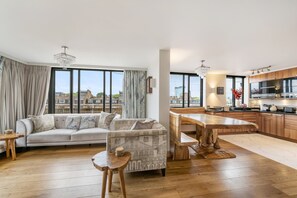 Eine moderne Wohnung mit Wohnzimmer, Essbereich und Küche, großen Fenstern und Blick auf die Stadt.